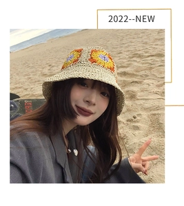 Close-up of bohemian woven straw bucket hat with colorful floral patterns on a beach