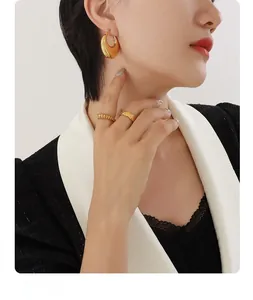 Close-up of polished gold U-shaped earrings and quilted texture rings on a model