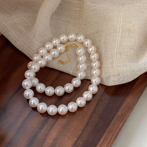 Detail of 10mm white pearl necklace with gold lobster clasp on linen and wood background