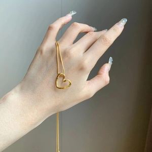 Collier avec pendentif cœur ajouré doré et chaîne maille serpent fine en gros plan à la main