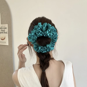 Close-up of model wearing a peacock green pleated silk scrunchie on a braided hairstyle