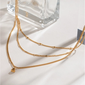 Three-layer gold stainless steel necklace with water drop pendant on a glass display