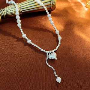 Detail of pearl choker necklace with heart pendant and tassel on brown silk