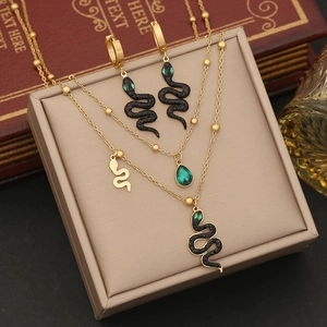Double-layered gold snake necklace and earrings set with green crystals on a jewelry box