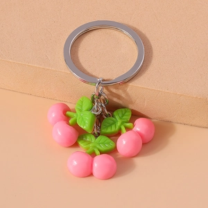Close-up of pink cherry-shaped keychain with green leaves on silver metal ring