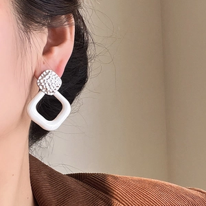 Close-up of geometric square earrings with silver hammered metal and white resin rings