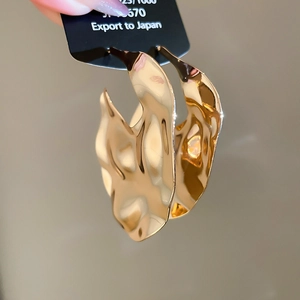 Close-up of gold metal hoop earrings with irregular hammered wavy texture on black card