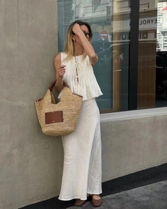 Detail of a handmade straw tote bag with leather handles and white linen pleated dress