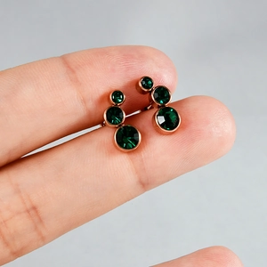 Gros plan de boucles d'oreilles or rose serties de cristaux vert émeraude