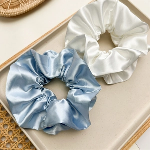 Close-up of blue and white satin scrunchies with pleated texture on a beige tray