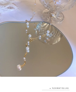 Detailed shot of a gold Y-shaped pearl necklace on a mirror with white feathers