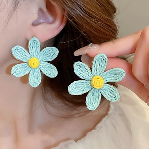 Détail de la boucle d'oreille fleur tressée bleue avec cœur jaune sur un mannequin