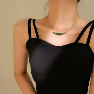 Close-up of gold snake chain necklace with green square-cut emerald-like stones