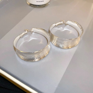 Macro detail of large silver-tone C-shape hoop earrings with a brushed metal texture finish