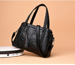 Detailed view of black quilted leather handbag with woven handles and fringe tassel charm