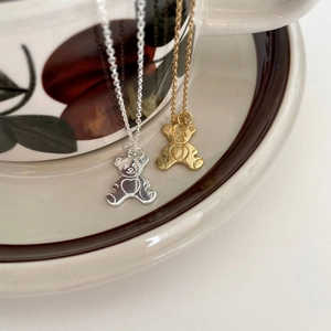 Elegant 925 sterling silver teddy bear necklaces in gold and silver finishes on a ceramic cup