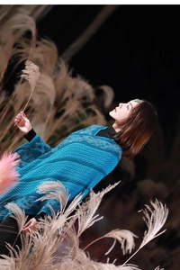 Artistic profile of a blue knitted poncho with fringe and diamond patterns on a model