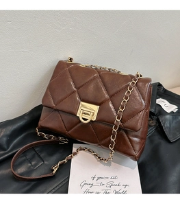 Detail of dark brown quilted flap bag with golden chain and twist lock on leather background