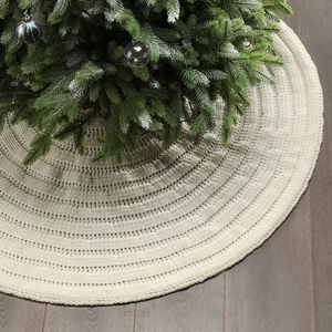 Detailed knit texture of cream white Christmas tree skirt on dark wood floor