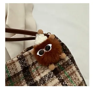 Detail eines süßen braunen Plüsch-Anhängers mit Sonnenbrille am karierten Shopper