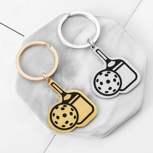 Pickleball paddle and ball metal keychains in gold and silver finishes on a marble tray