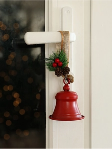 Detail of red metal Christmas bell with pine needles and berries hanging on a door handle