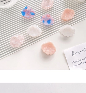 Detailed macro view of shell-shaped acetate hair clips in assorted colors on a textured surface