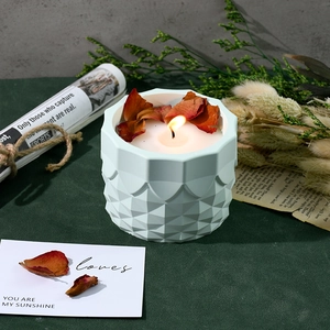 Detailed view of white geometric lotus candle with red dried flower petals and lit flame
