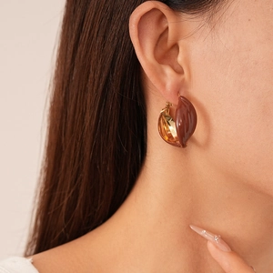 Close-up of minimalist gold-plated C-shaped earrings with dark red enamel on a model