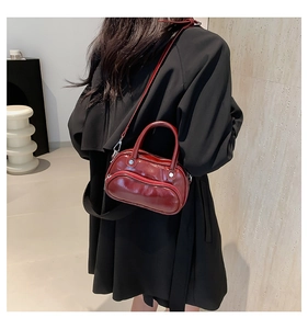 Detail of dark burgundy patent leather crossbody bag with silver hardware and top handles