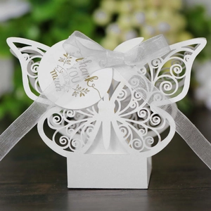 Close-up of white laser-cut butterfly favor box with ribbon and gold-lettered tag