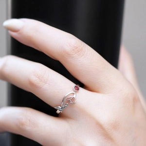 Detail of silver floral ring featuring an open-band design and a red zircon stone centerpiece