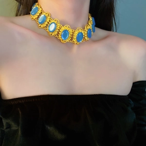 Detail of vintage gold necklace with blue oval stones on a model wearing black velvet