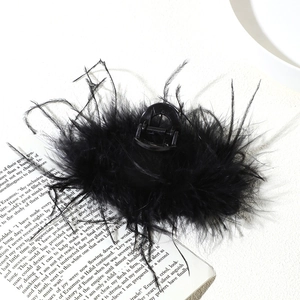 Top view of a fluffy black ostrich feather hair claw clip on an open vintage book page