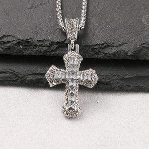 Macro detail of silver cross pendant with sparkling zircons on dark textured rock surface