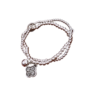 Double-layered beaded silver bracelet with flower charm and bell on white background