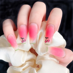Detail of pink gradient coffin nails with cherry pattern holding a white silk scrunchie