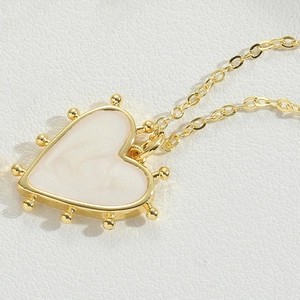 Macro detail of gold heart pendant with white enamel inlay and beaded edge design