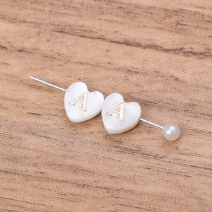Détail d'une perle en nacre en forme de cœur avec lettre A dorée et petite perle