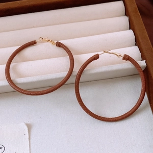 Macro detail of brown leather wrapped hoop earrings with golden clasp in a velvet box