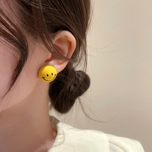 Close-up of a vibrant yellow round button earring featuring a classic black smiley face