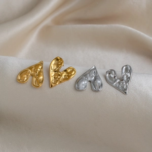 Boucles d'oreilles cœur texture lave dorées et argentées sur un élégant tissu en soie beige