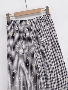 Détail du pantalon à carreaux noir et blanc avec broderie florale blanche et taille élastique
