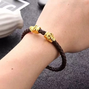 Detail of hand wearing a braided brown leather punk bracelet with gold skull accents