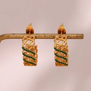 Détail de boucles d'oreilles créoles dorées ajourées avec zircons verts sur un support