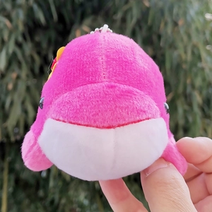 Detailed view of a cute pink and white plush whale keychain held in hand against greenery
