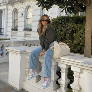 Olive green bomber jacket styled with light blue wide-leg jeans and a beige tote bag