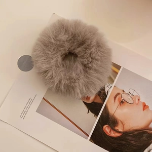Detail of soft grey faux fur hair tie placed on a lifestyle magazine backdrop