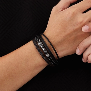 Detailed close-up of multilayered black and brown leather bracelet with metal arrow pendant