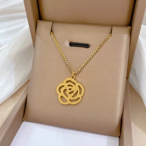 Collier minimaliste en acier titane doré avec pendentif rose camélia évidé dans sa boîte